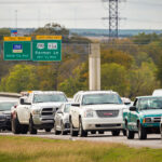 Slow-moving traffic approaching Highway 290 toll road signs showing Parmer Lane exit information