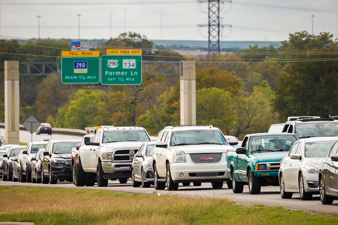 Slow-moving traffic approaching Highway 290 toll road signs showing Parmer Lane exit information