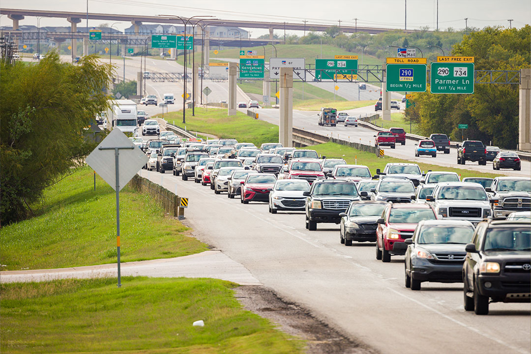 Heavy daytime traffic on Highway 290 with toll road signage and overpass infrastructure visible