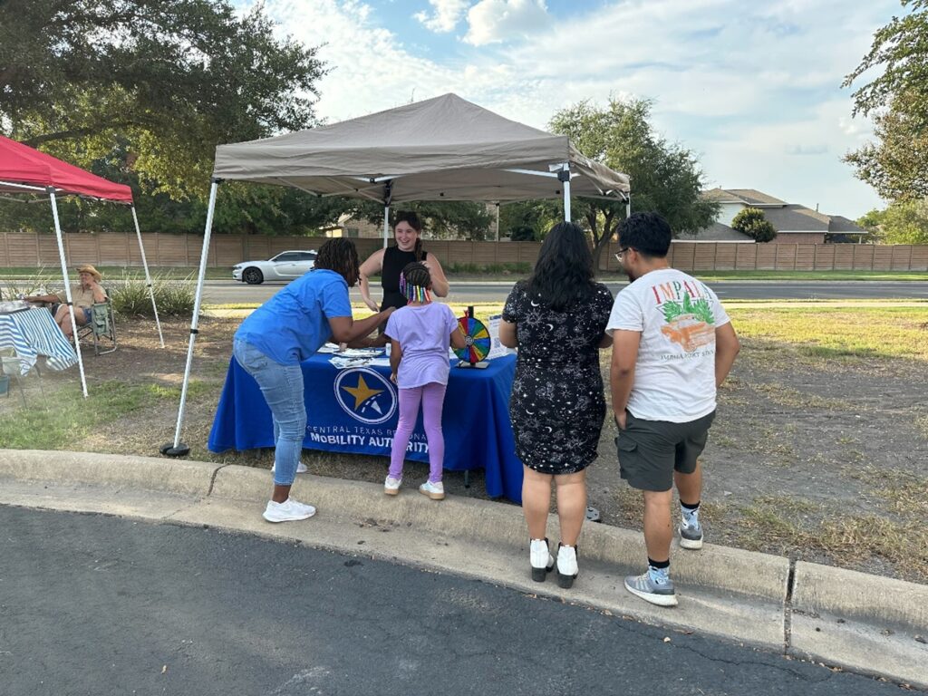 A member of the 290 Extension Project team interacting with the public at a booth set up at the Manor Farmer's Market.