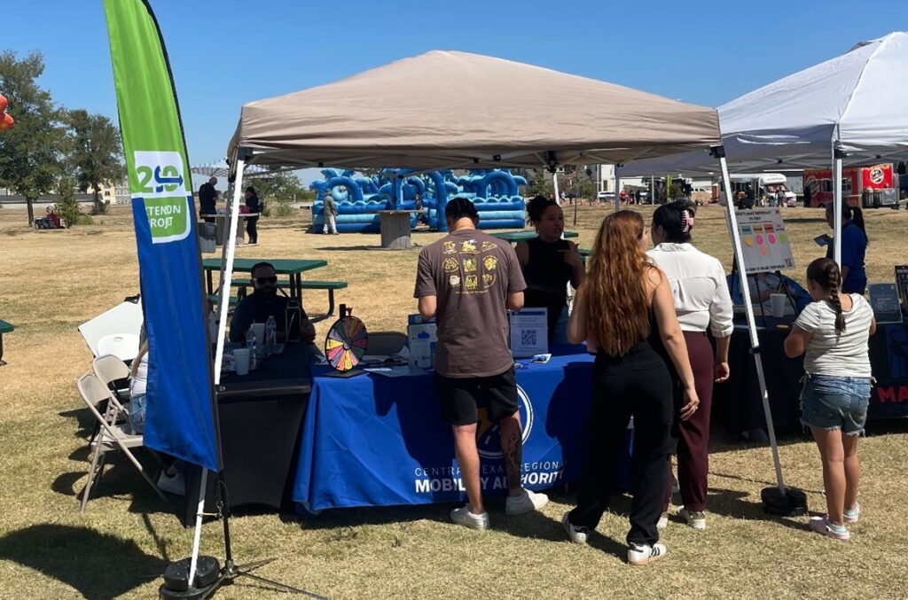 A member of the 290 Extension Project team interacting with the public at a booth with information and giveaways.